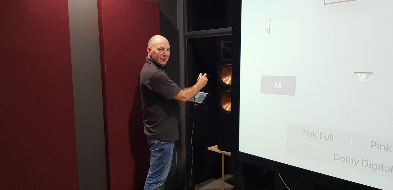 Home theatre engineer inspecting a speaker installation beside a projection screen